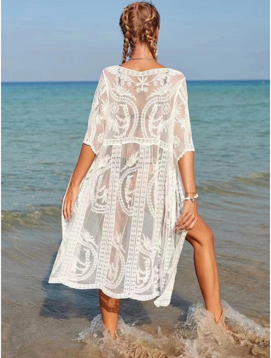 A woman wearing a white kimono with a lace pattern is standing at the beach. You can see through the kimono slightly.