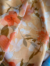Load image into Gallery viewer, A scarf is shown. It has a orange flower pattern on it and has a white silhouettes of flowers and leaves. The background of the scarf is a peach colour. The fabric is light and slightly see through. 
