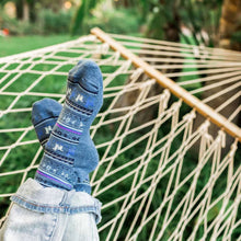 Load image into Gallery viewer, Feet with blue socks is shown on a hammock outside.
