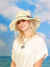 Load image into Gallery viewer, A woven white hat with brown string around the rim is shown on a woman in front of a beach backdrop.
