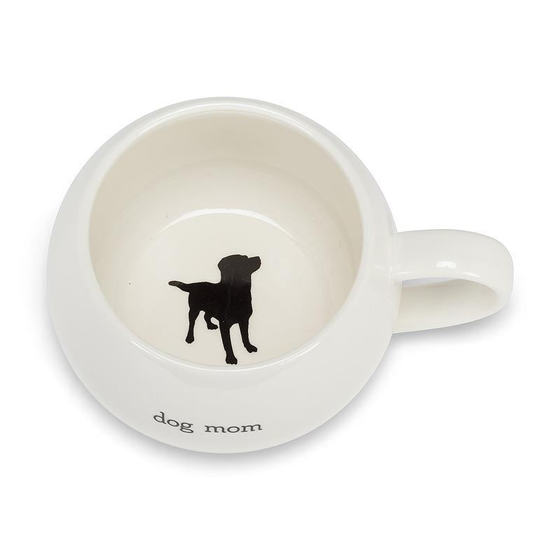 A white round mug is shown with a black silhouette of a dog in the bottom of the mug. On the side has the words dog mom.